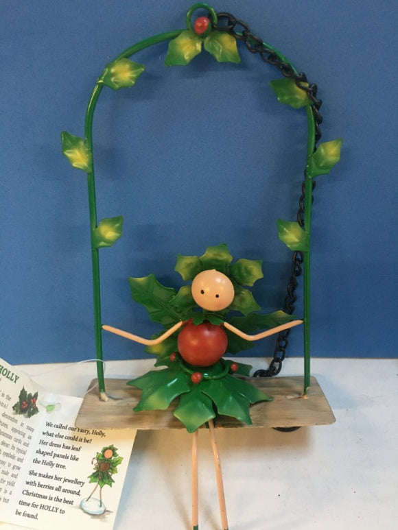 metal fairy sitting on a swing decorated with holly